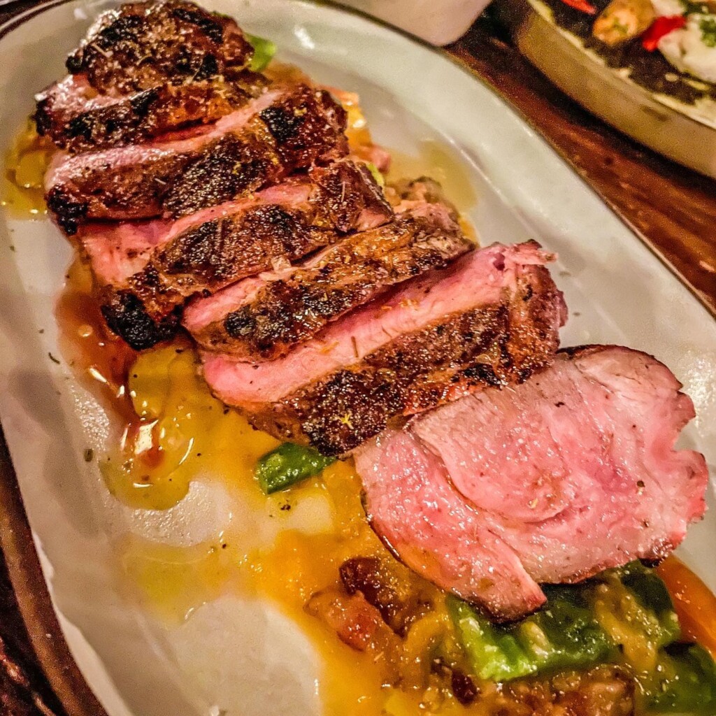 Sliced bone-in ribeye steak served on a plate with vibrant sauces and vegetables, highlighting La Lupa's elevated Italian steakhouse offerings.