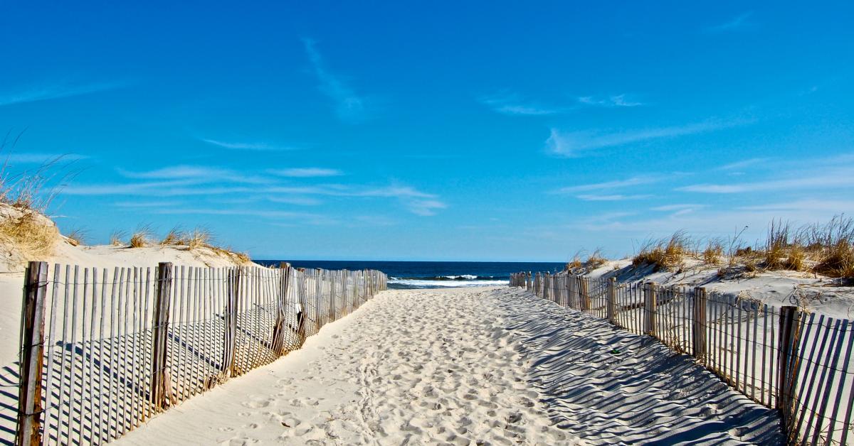 Pathway leading to the beach with sand dunes and wooden fencing under a clear blue sky, symbolizing the natural beauty of Island Beach State Park near Seaside Heights.