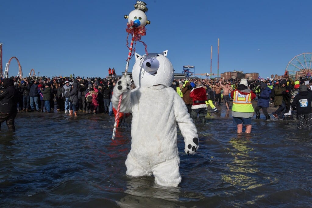 Polar Bear mascot holding a festive staff in icy ocean waters, surrounded by enthusiastic participants at the Polar Bear Plunge 2025 in Seaside Heights, NJ.