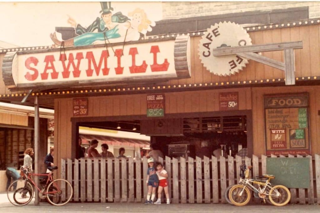 Sawmill pizzeria on Seaside Park boardwalk, featuring iconic sign, wooden fence, and patrons enjoying pizza, capturing local dining experience and history.