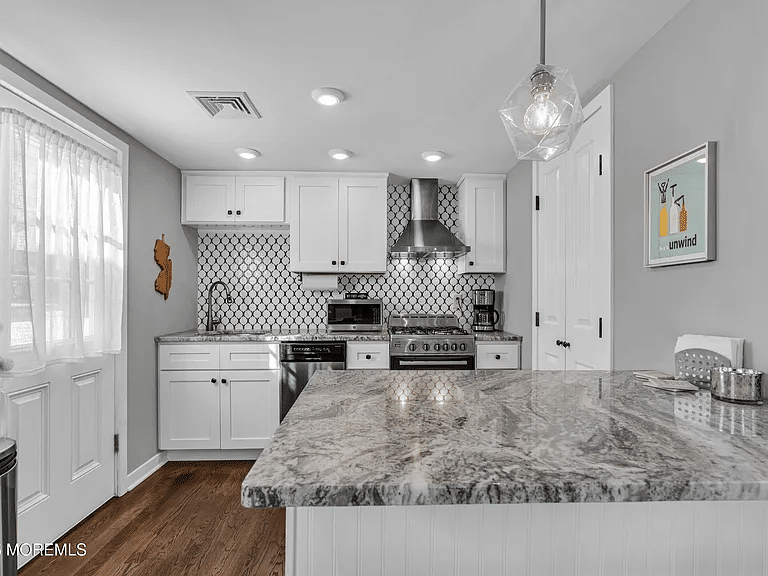 Modern kitchen with white cabinetry, granite countertop, stainless steel appliances, hexagonal backsplash, and decorative elements, reflecting coastal living and work-from-home lifestyle at the Jersey Shore.