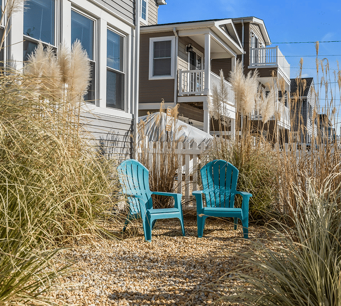 Cozy turquoise Adirondack chairs in a sandy garden surrounded by tall grasses, near beach houses at the Jersey Shore, ideal for vacation rental relaxation.