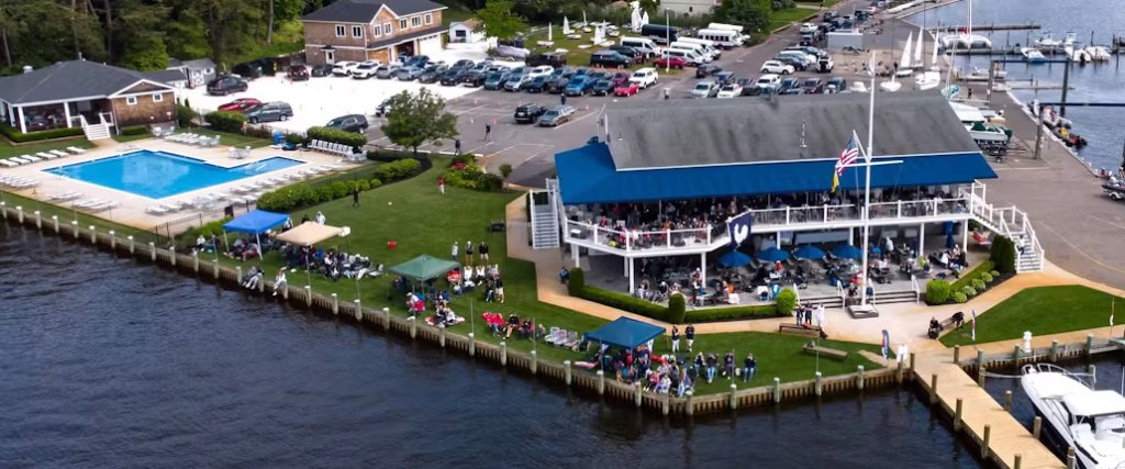 Aerial view of Toms River Yacht Club featuring the main building with outdoor seating, pool area, and event setup along the waterfront, highlighting the club's vibrant community atmosphere and scenic location.