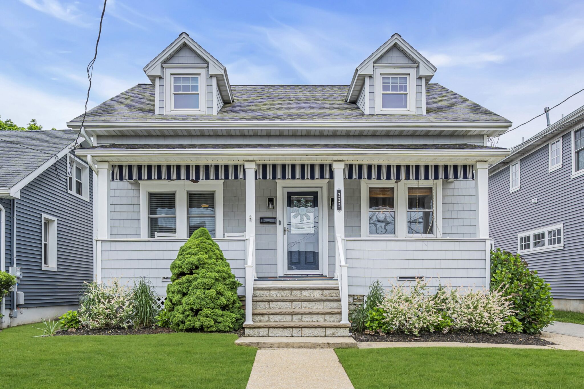Charming beach house with a front porch, manicured lawn, and coastal architecture, ideal for vacation rentals at the Jersey Shore.