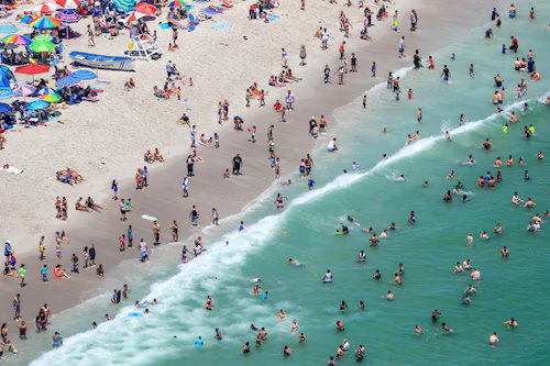 Crowded Seaside Heights beach with umbrellas and people swimming in the ocean.