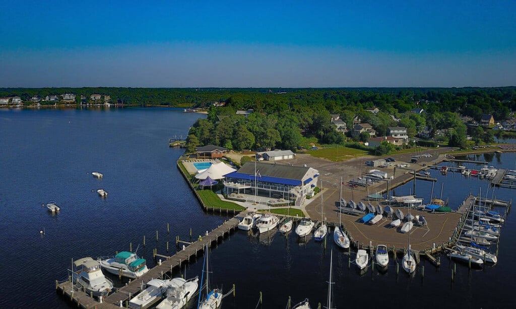 Aerial view of Toms River Yacht Club featuring boat slips, docked sailboats, and the club's waterfront facilities amidst lush greenery, highlighting its prime location for sailing and social events.