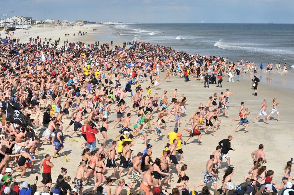 Crowd of participants running into the ocean during the Polar Bear Plunge event in Seaside Heights, showcasing community spirit and winter dare excitement.