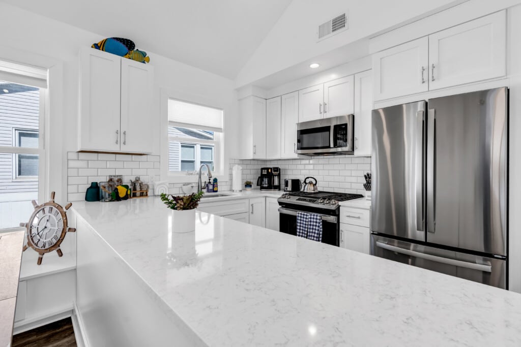 Modern kitchen with white cabinets, stainless steel appliances, and a marble countertop, featuring a decorative clock and colorful accents, ideal for vacation rentals at the Jersey Shore.