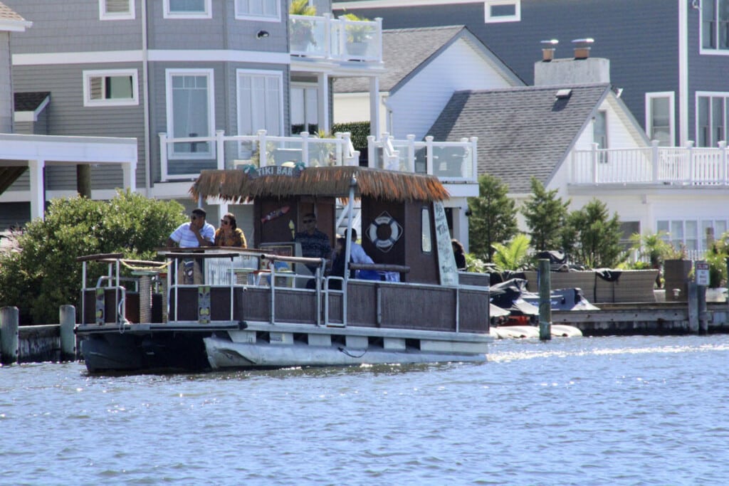 Tiki bar pontoon boat on the water, surrounded by waterfront homes, offering a scenic cruise experience in Seaside Heights.