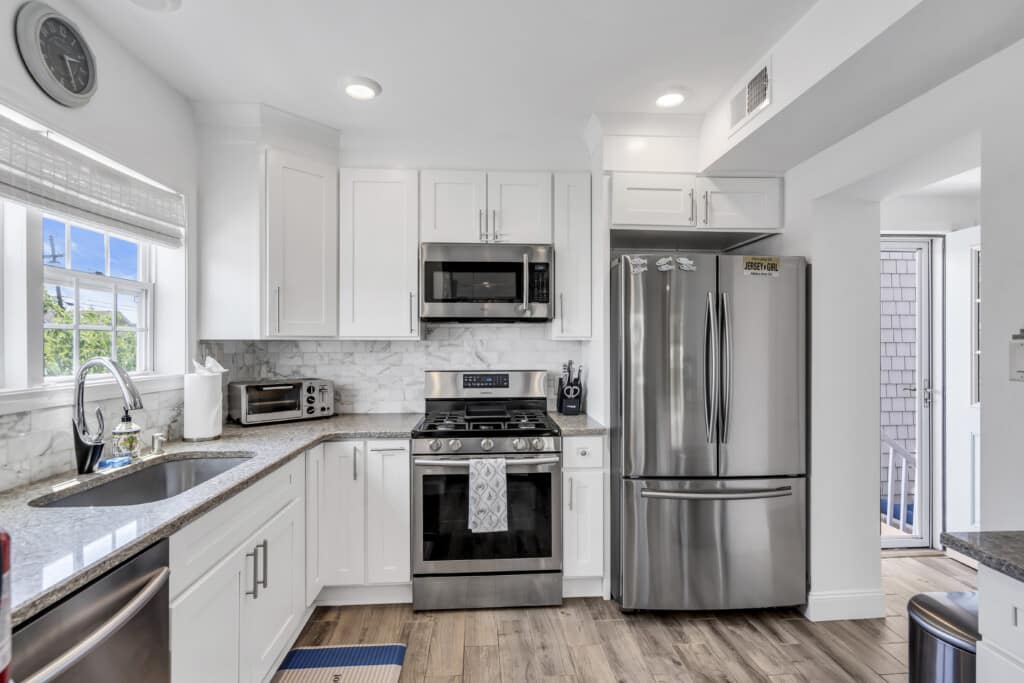Modern kitchen with stainless steel appliances, white cabinetry, and granite countertops, showcasing a rental-friendly space ideal for vacationers in Jersey Shore towns.