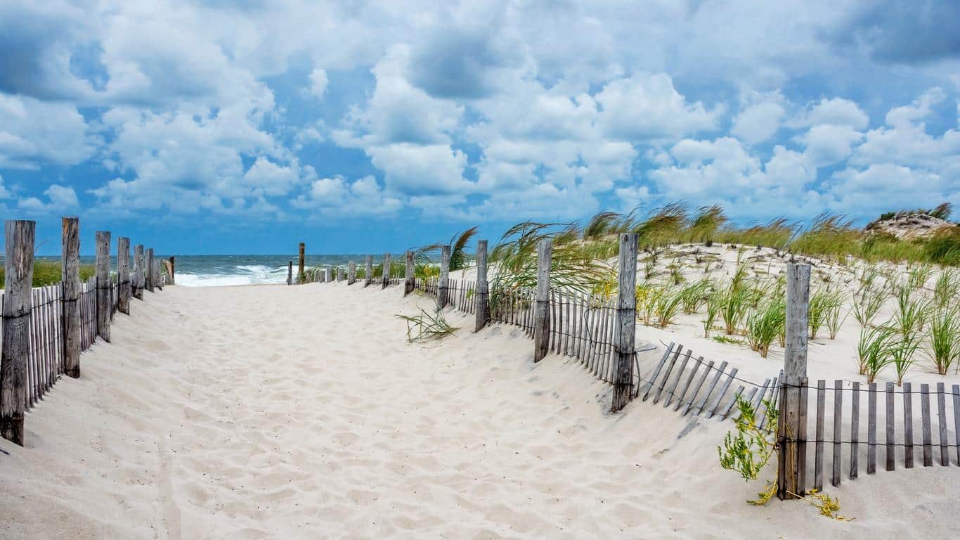 Pathway leading to Seaside Park beach with wooden fencing, sandy dunes, and a cloudy sky, representing a tranquil Jersey Shore vacation spot.