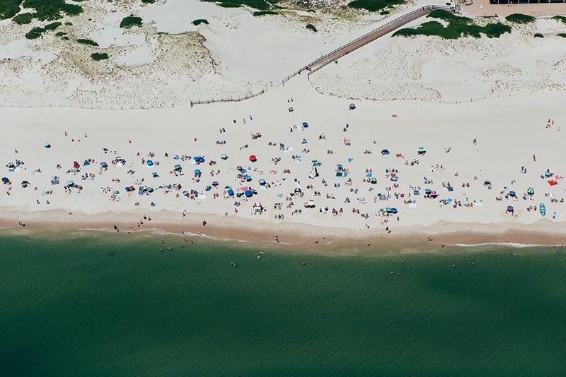 Aerial view of a busy dog-friendly beach with colorful umbrellas, sunbathers, and swimmers enjoying the water near Seaside Heights, ideal for pet owners seeking vacation activities.
