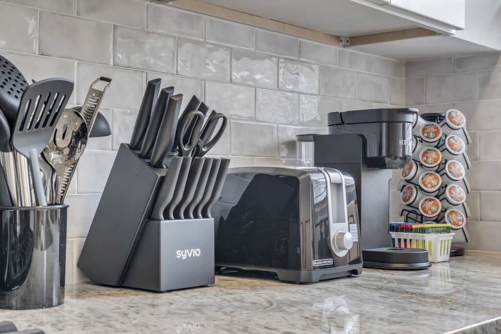 Kitchen countertop featuring black kitchen utensils, a knife block labeled "SYVIO," a toaster, and a coffee maker with a pod holder, emphasizing modern amenities for vacation rentals.