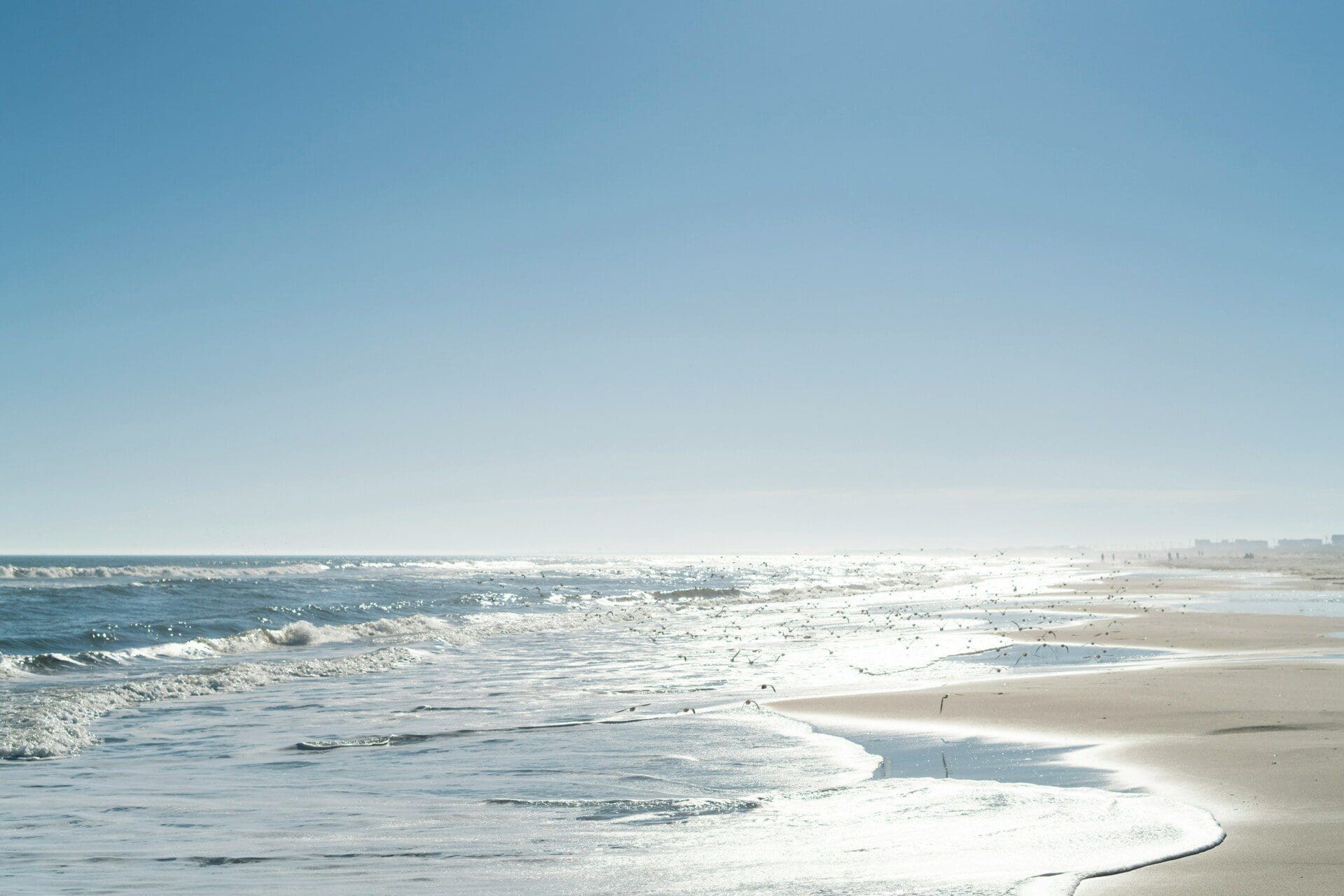 Jersey Shore beach scene with gentle waves, sunlit sands, and a clear blue sky, reflecting the vibrant coastal charm and inviting atmosphere described in the Breezy Beach Stays guide.