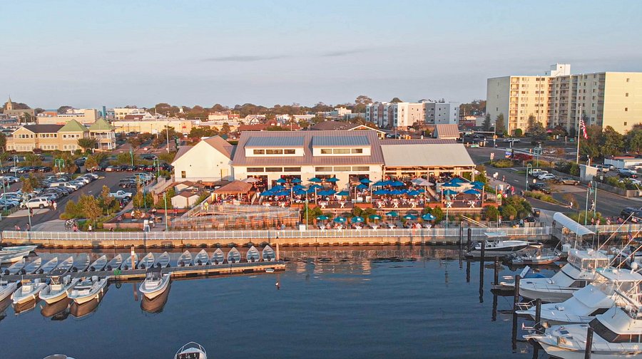 Aerial view of a waterfront restaurant with outdoor seating, blue umbrellas, and boats docked nearby, showcasing the inviting atmosphere for dining at the Jersey Shore.
