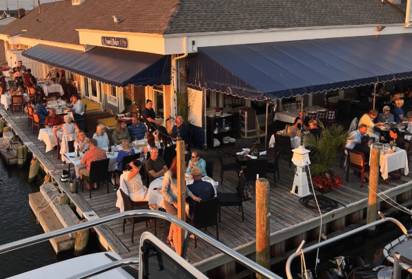 Outdoor dining at Channel Marker Cafe, patrons enjoying meals on the waterfront, sunset ambiance, scenic views of the bay, relaxed atmosphere.