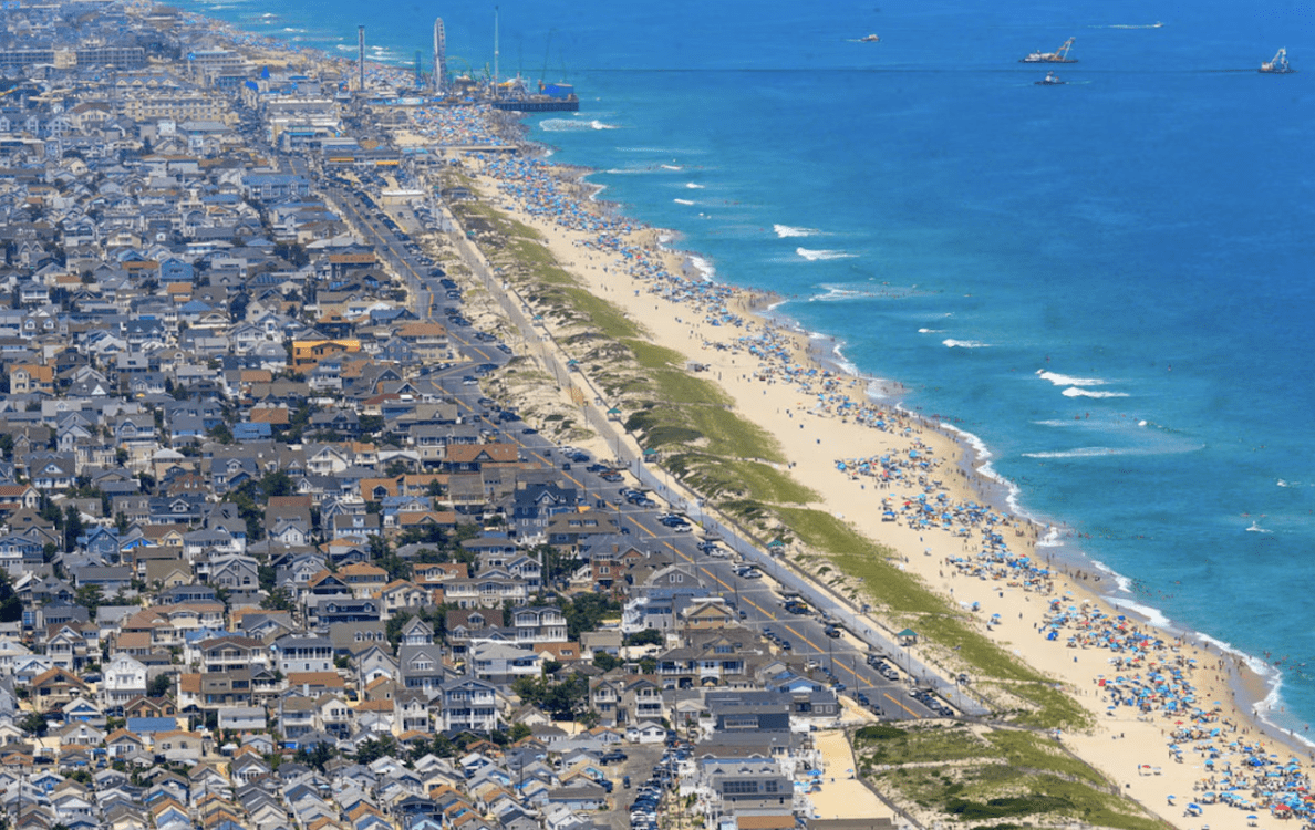 Aerial view of Seaside Heights, NJ, showcasing vibrant beach, crowded shoreline with umbrellas, and nearby boardwalk attractions, reflecting the lively atmosphere of summer activities at the Jersey Shore.