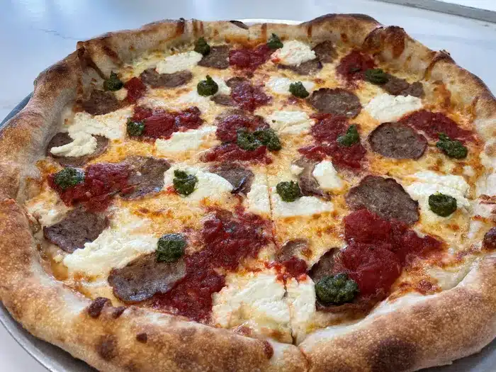 Vodka sauce pizza topped with ricotta, meat, and dollops of pesto, showcasing Pacidough's signature dish in Toms River.