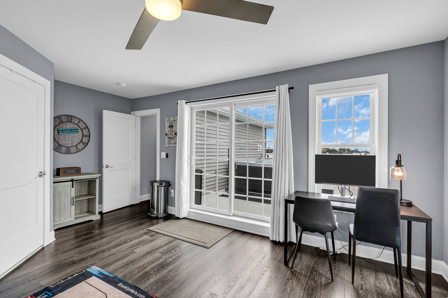 Bright and modern vacation rental interior featuring a workspace with a computer, two chairs, and large windows showcasing outdoor views, ideal for Jersey Shore property management.