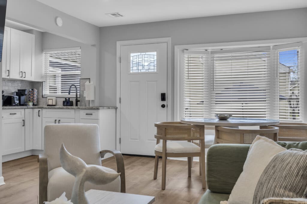 Modern beach house interior with cozy seating, dining area, and kitchen featuring white cabinetry, promoting Breezy Beach Stays vacation rentals at the Jersey Shore.