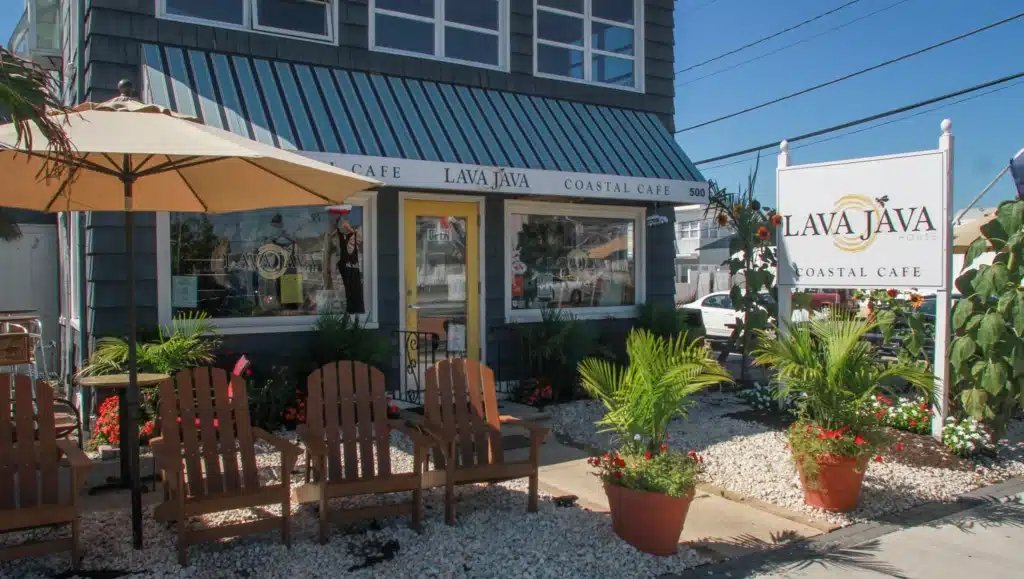 Lava Java Coastal Café exterior in Lavallette, featuring a welcoming entrance, outdoor seating with wooden chairs, and a sign showcasing the café's name, surrounded by tropical plants and a relaxed atmosphere.