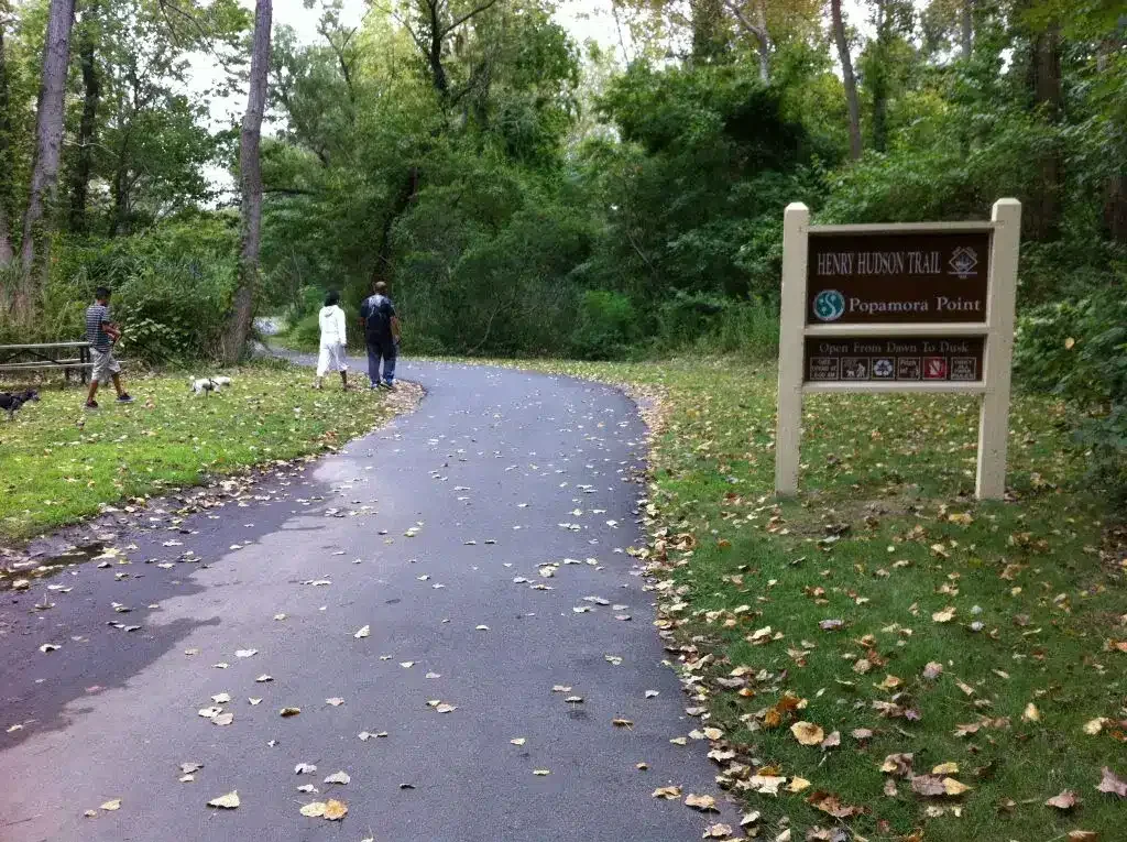 Henry Hudson Trail sign at Popamora Point with a paved path surrounded by greenery.