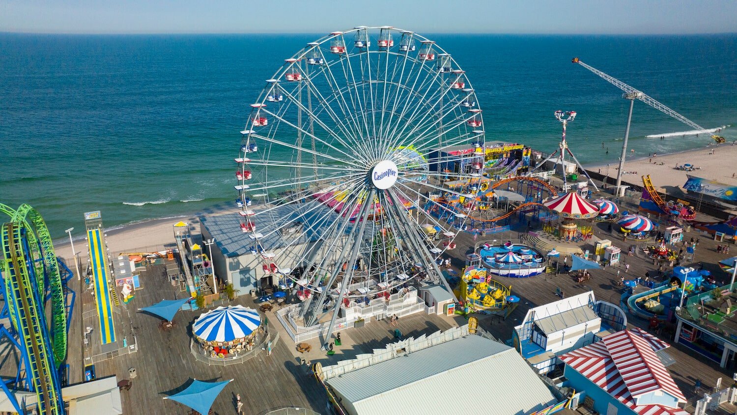 Ferris wheel at Casino Pier in Seaside Heights, with colorful amusement rides and beach in background.