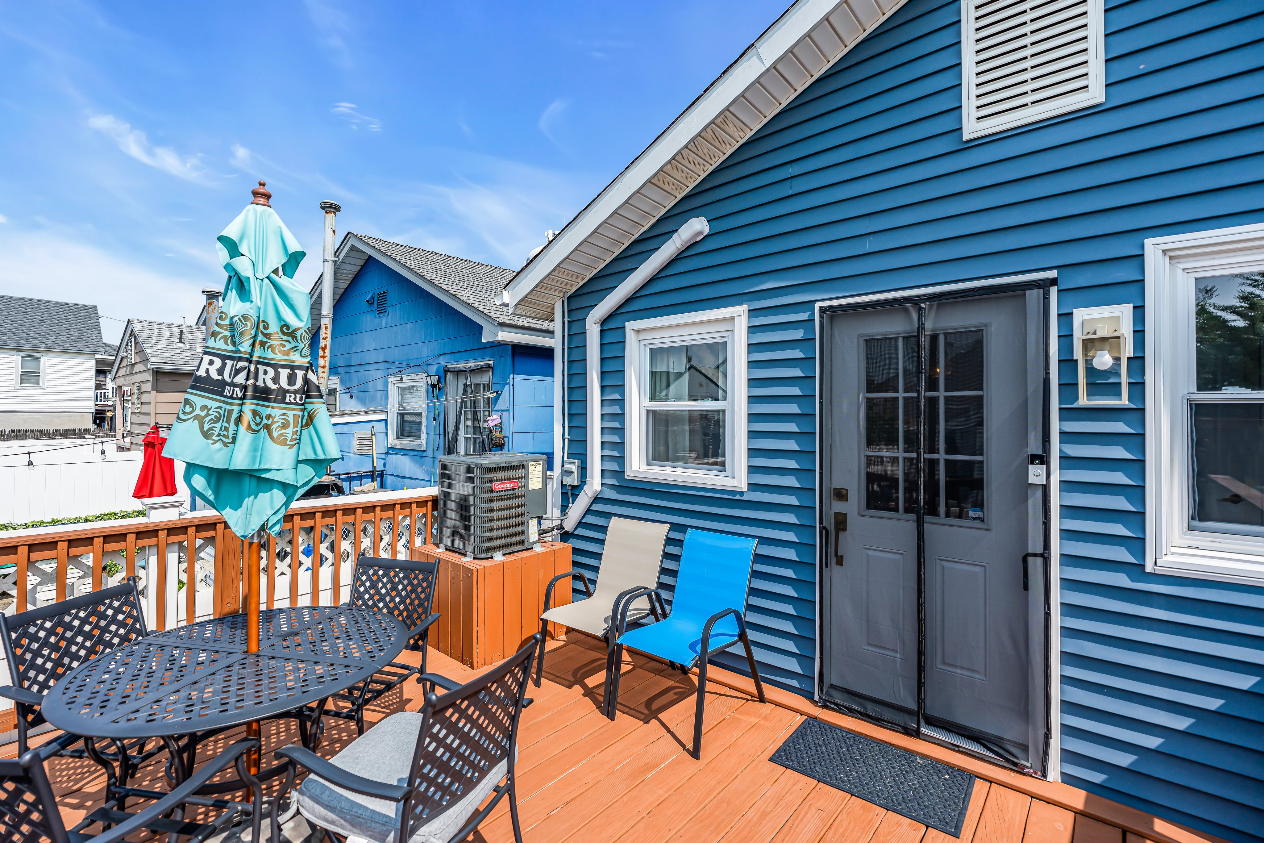Cozy outdoor patio with a round table and chairs, featuring a turquoise umbrella, adjacent to a blue beach house, ideal for vacation rentals at the Jersey Shore.