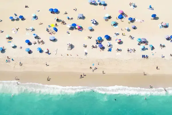Crowded Spring Lake beach with colorful umbrellas, sunbathers, and gentle waves.