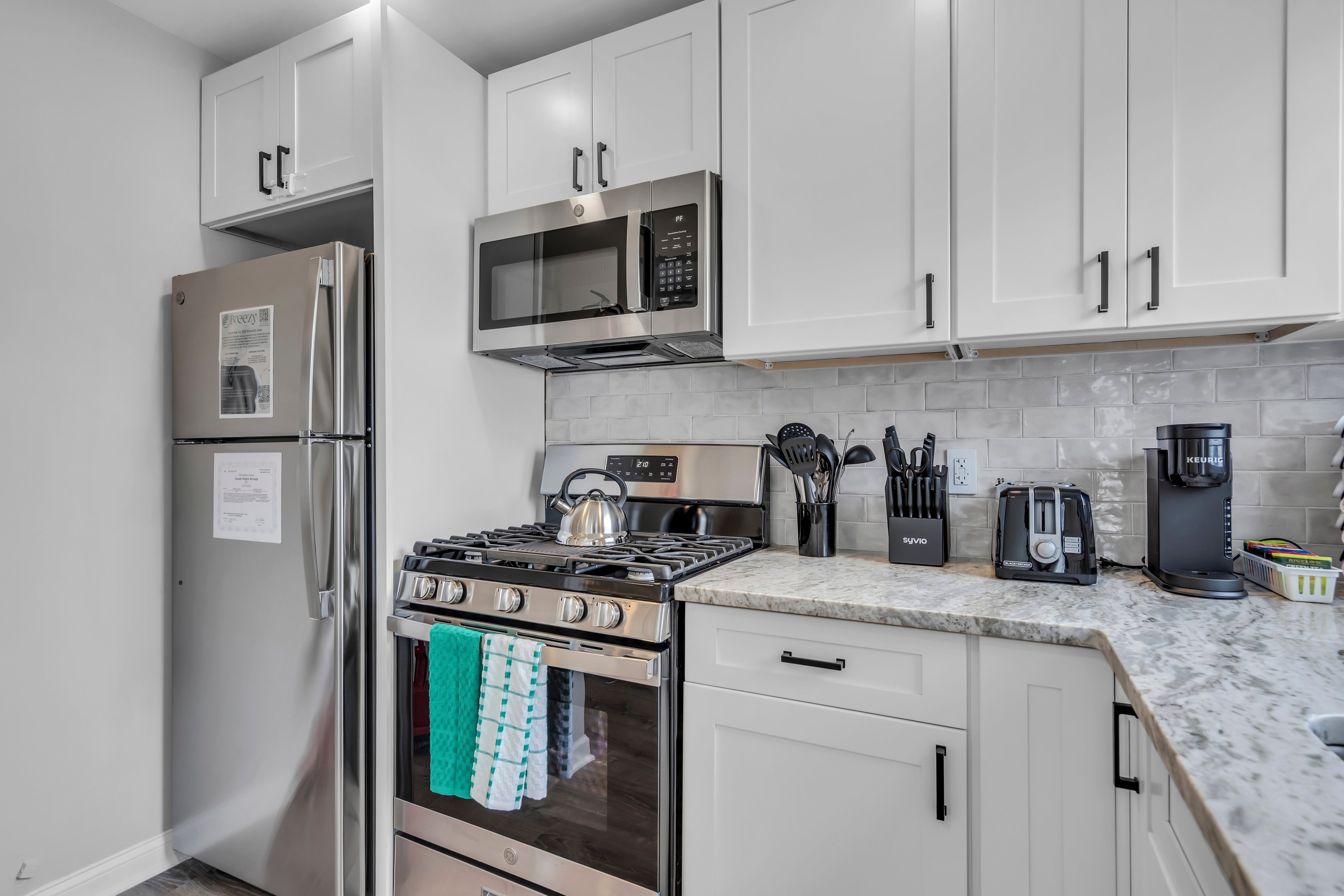 Modern kitchen with stainless steel appliances, including a refrigerator, microwave, and gas stove, showcasing coastal-themed decor and maintenance-friendly surfaces.
