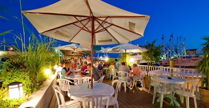 Outdoor dining at The Shrimp Box, featuring tables under umbrellas and a waterfront view with boats.