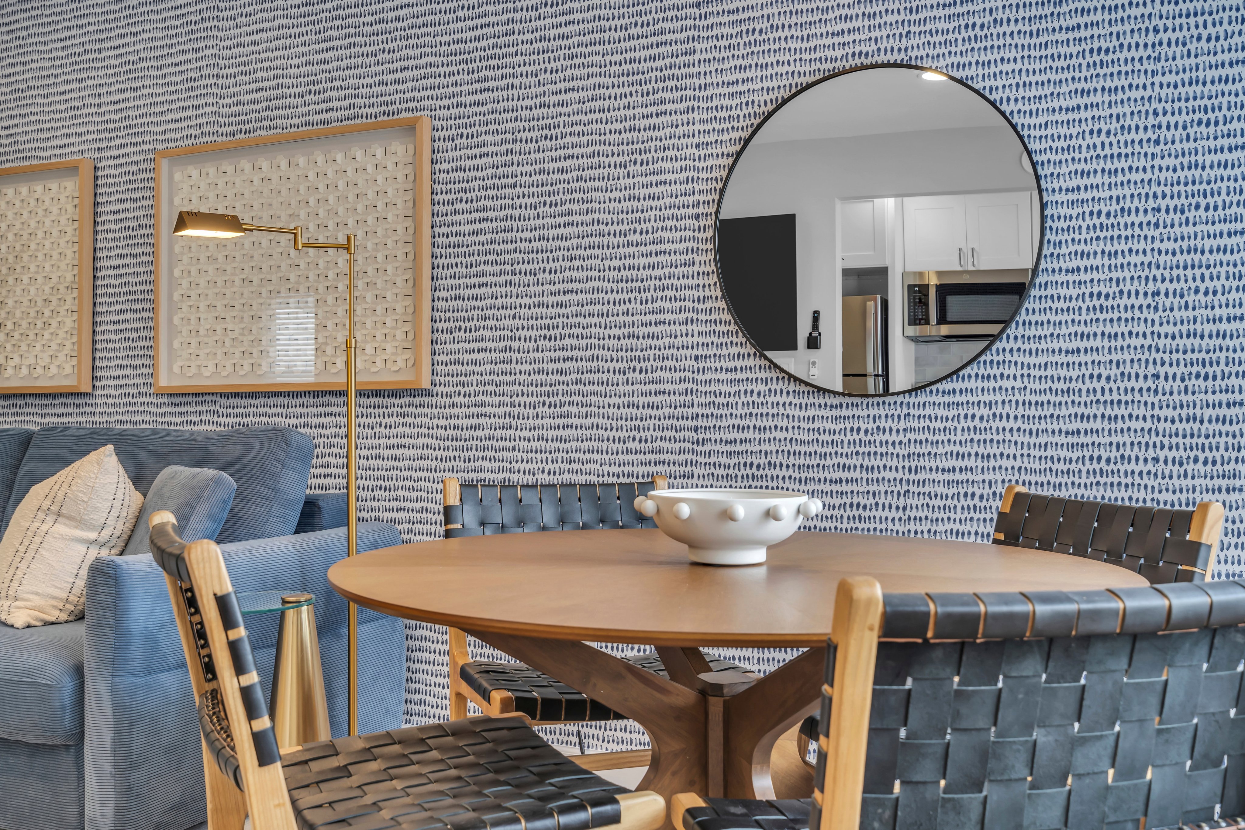 Cozy dining area with round wooden table, woven chairs, modern lamp, decorative wall art, and circular mirror, showcasing a stylish Jersey Shore vacation rental interior.