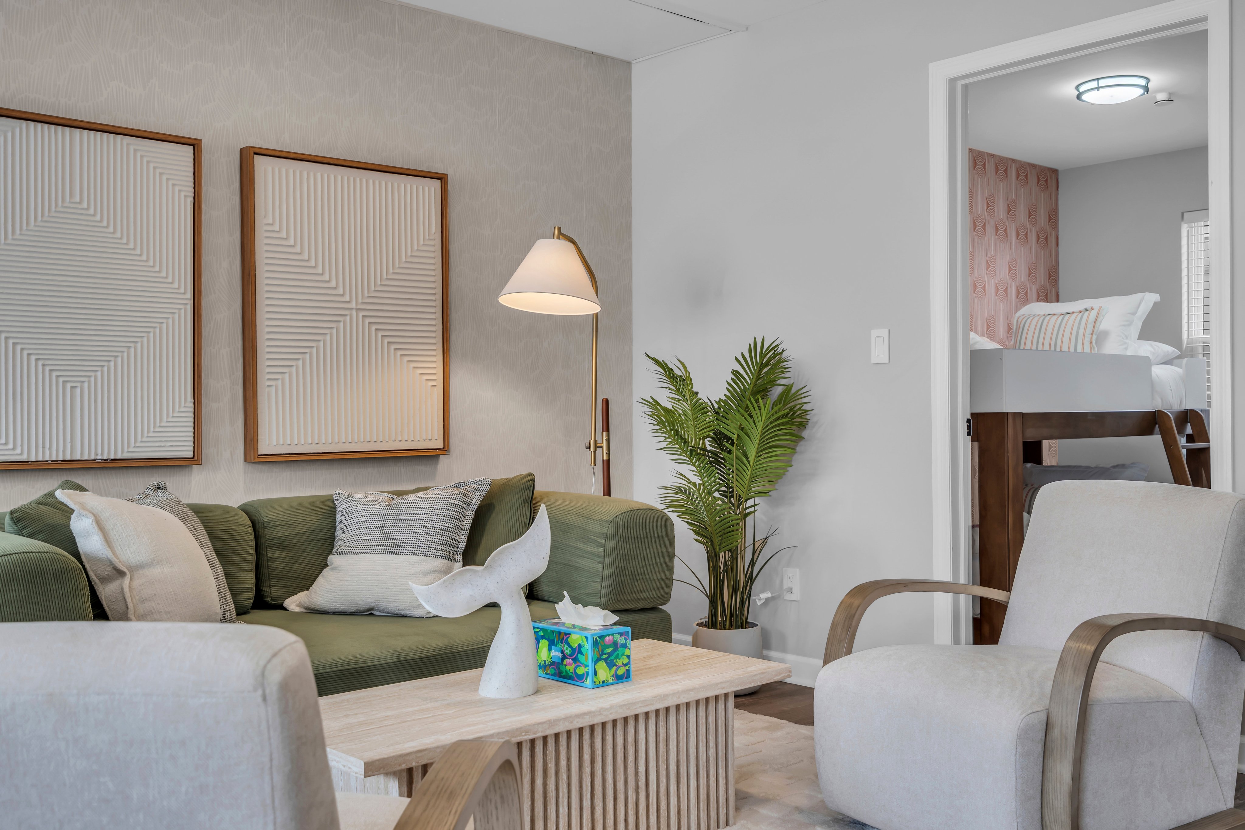 Cozy living room in a shore rental, featuring green sofa with decorative pillows, modern art on walls, stylish lamp, and tropical plant.