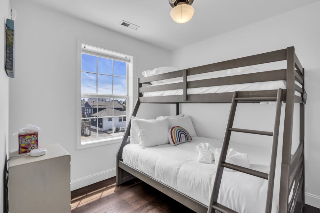 Cozy bedroom with bunk beds, large window providing natural light, and colorful decorative pillow, ideal for family vacations at the Jersey Shore.