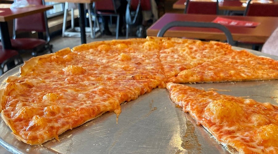 Thin crust pizza on a metal serving tray, with melted cheese and tomato sauce, showcasing a slice being pulled away, in a casual dining setting at a Jersey Shore pizzeria.