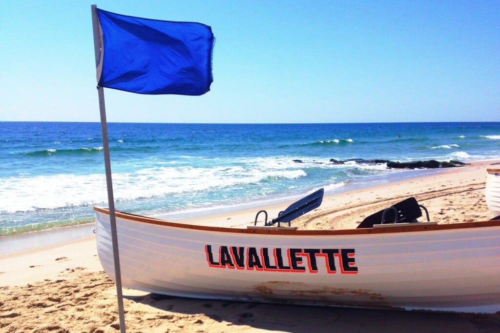 Lavallette beach boat with blue flag, sandy shore and ocean waves, representing coastal living and community spirit at the Jersey Shore.