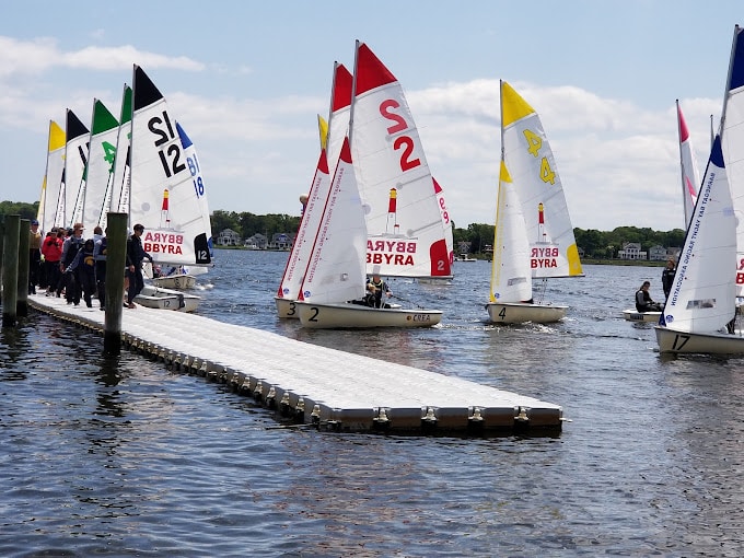 Sailboats with colorful sails on the water near Toms River Yacht Club, with participants preparing for sailing activities on a sunny spring day.