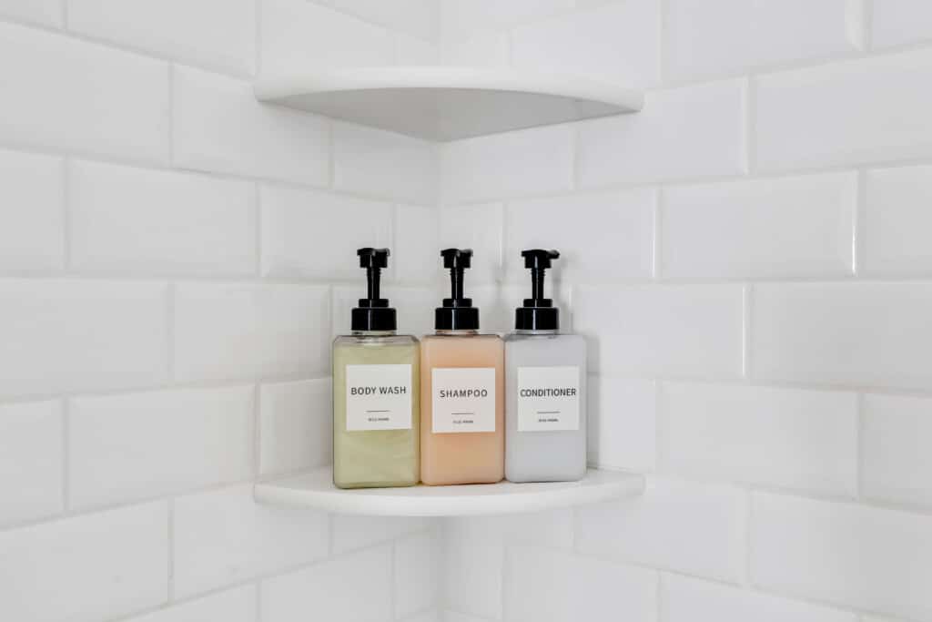 Body wash, shampoo, and conditioner bottles on a shelf in a clean, white tiled shower, emphasizing guest amenities for vacation rentals at the Jersey Shore.