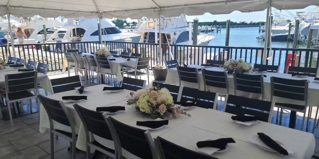 Waterfront dining setup with tables adorned with floral centerpieces, overlooking boats on the Manasquan River, reflecting the relaxed yet refined atmosphere of coastal dining experiences at Jersey Shore restaurants.
