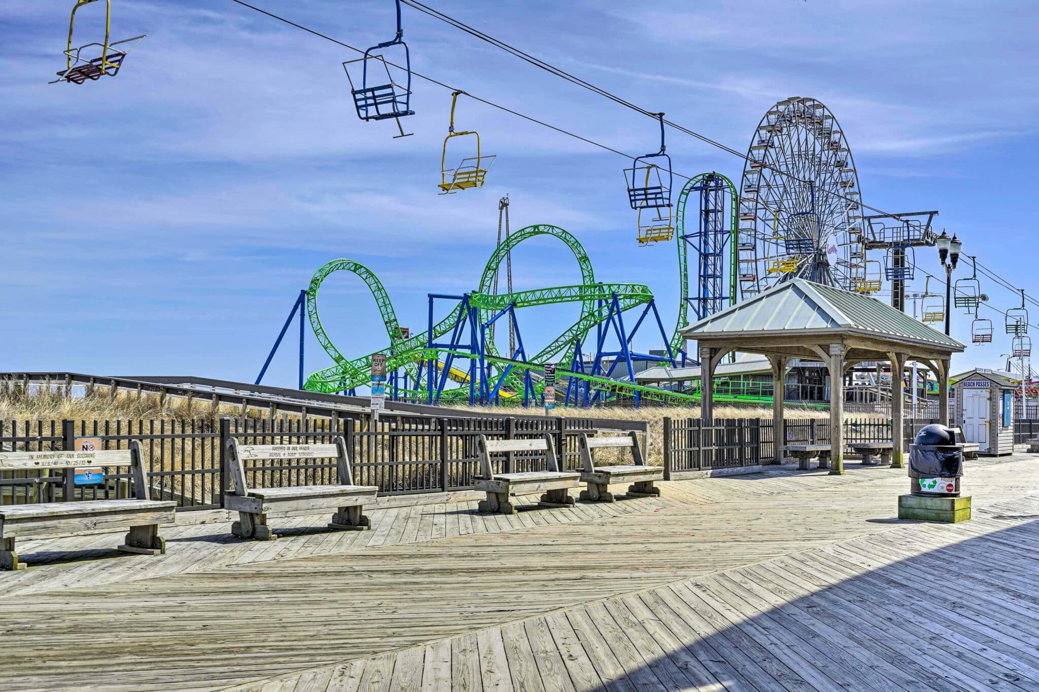 Jersey Shore boardwalk featuring colorful amusement rides, including a roller coaster and Ferris wheel, with wooden benches and a gazebo in the foreground, capturing the vibrant atmosphere of seaside entertainment.