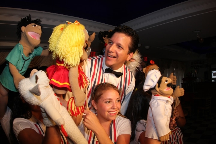 Performers with puppets in a vibrant ice cream shop, showcasing a nostalgic atmosphere with live entertainment.