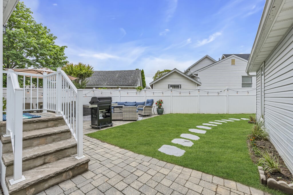 Backyard patio area at the Jersey Shore featuring stone steps, a green lawn, outdoor seating, and a grill, emphasizing outdoor living and investment potential for home buyers.