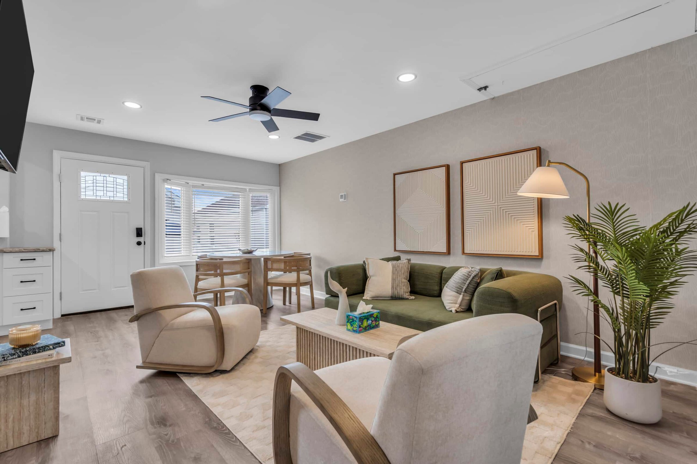 Modern living room with green sofa, beige chairs, dining table, and decorative plants, showcasing inviting atmosphere for vacation rental at the Jersey Shore.