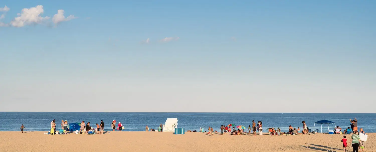 Beach scene at Jersey Shore with people enjoying the sun, colorful umbrellas, and the Atlantic Ocean in the background, illustrating a perfect beach day experience.