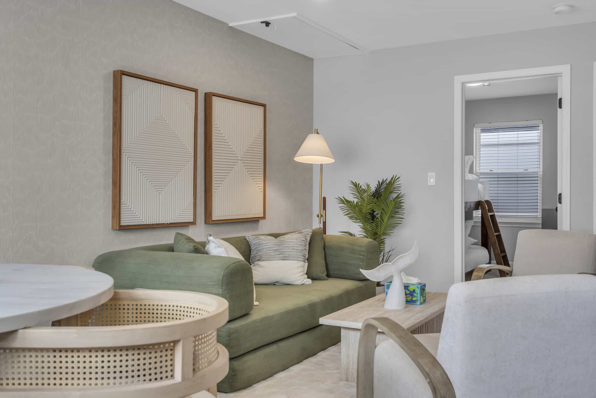 Cozy living room in a vacation rental, featuring a green sofa, modern artwork, and a light fixture, with a glimpse of a bedroom in the background, highlighting Jersey Shore investment potential.
