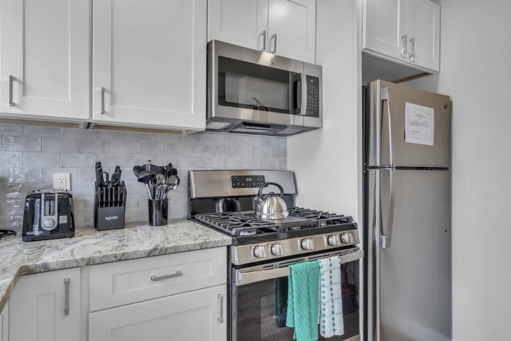 Modern kitchen with stainless steel appliances, including a gas stove, microwave, and refrigerator, featuring granite countertops and organized utensils, ideal for vacation rentals at the Jersey Shore.