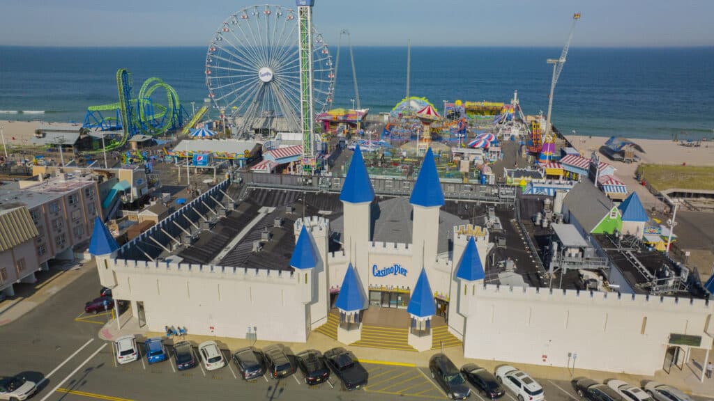 Casino Pier amusement park in Seaside Heights, featuring colorful rides, a large Ferris wheel, and beach views, with a castle-like entrance marked by blue turrets.