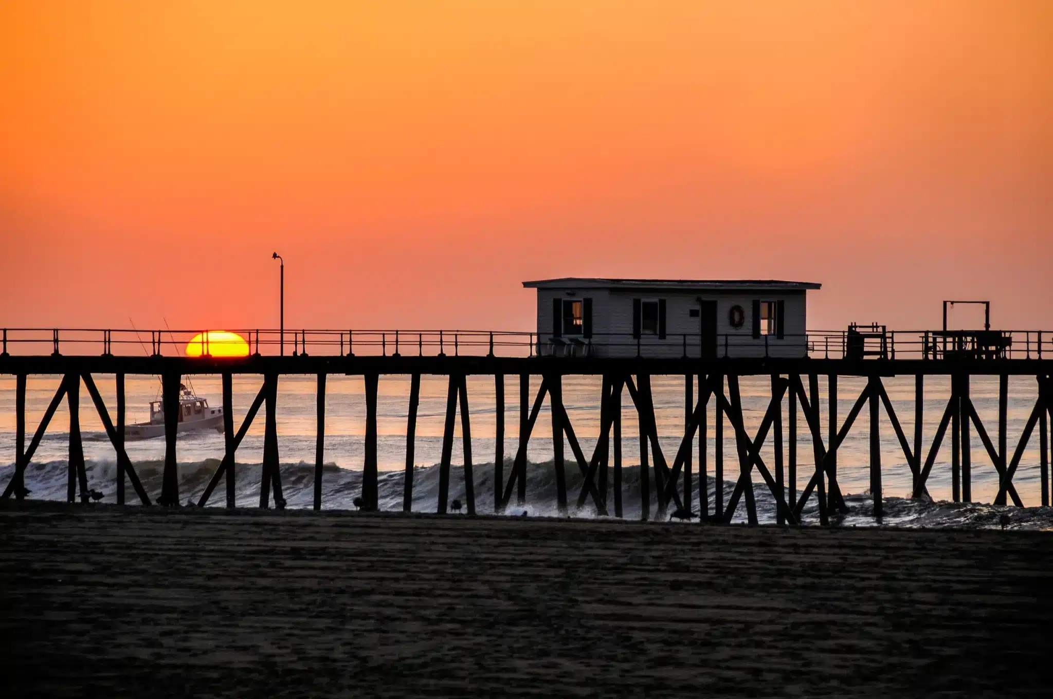 Sunset over Belmar beach pier with lifeguard station and fishing boat, highlighting the town's family-friendly coastal atmosphere.