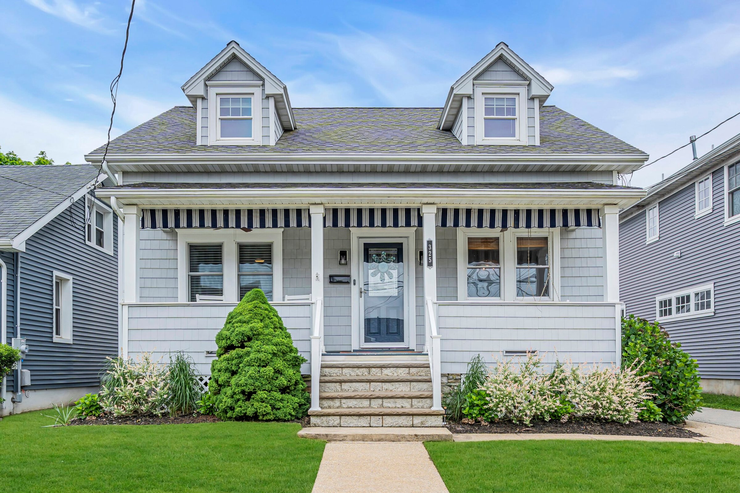 Charming coastal house with gray siding and white trim, featuring a front porch, steps leading to the entrance, and landscaped garden, ideal for Jersey Shore vacation rentals.