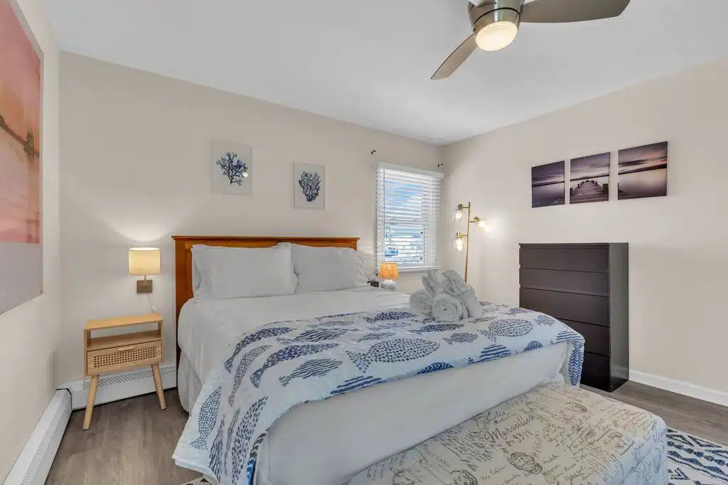 Cozy beach rental bedroom with ocean-themed decor, queen bed, bedside lamp, and dresser, emphasizing relaxing coastal atmosphere ideal for vacationers.
